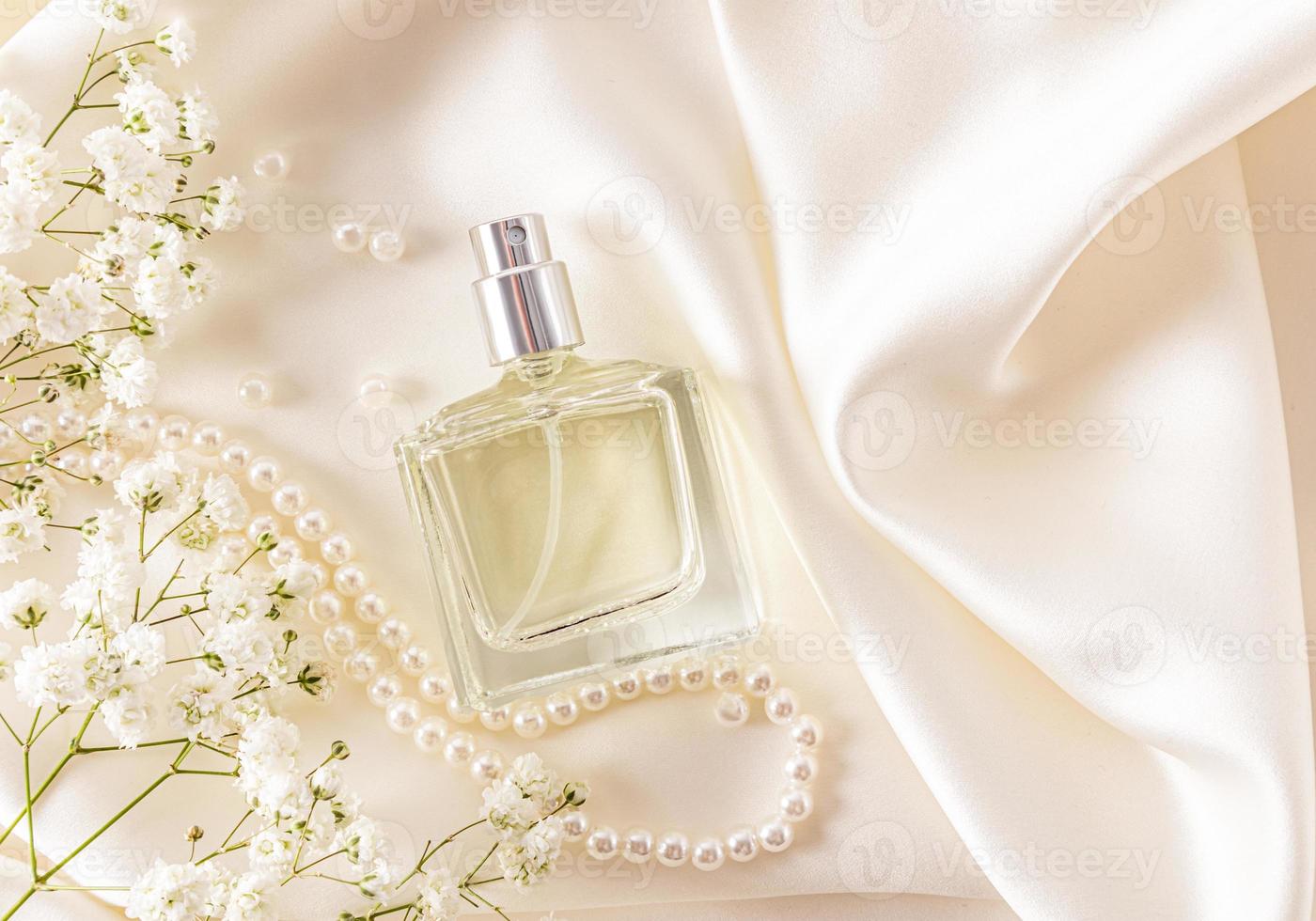 un élégant flacon de parfum féminin sur tissu atlas couleur ivoire avec gypsophile blanche et perles. odeur sensuelle. vue de dessus. photo