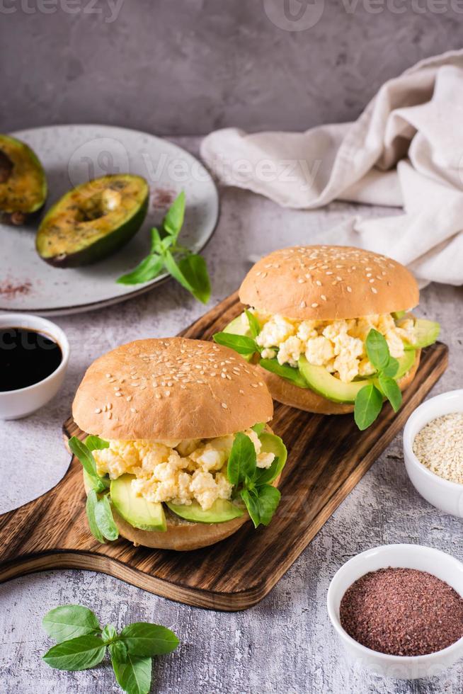 hamburger à l'avocat, œufs brouillés et basilic sur une planche sur la table. nourriture saine. vertical photo