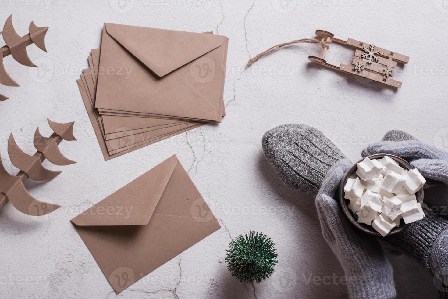 les mains féminines dans les gants tiennent du cacao avec des guimauves, des enveloppes artisanales et des arbres de noël. vue de dessus. photo