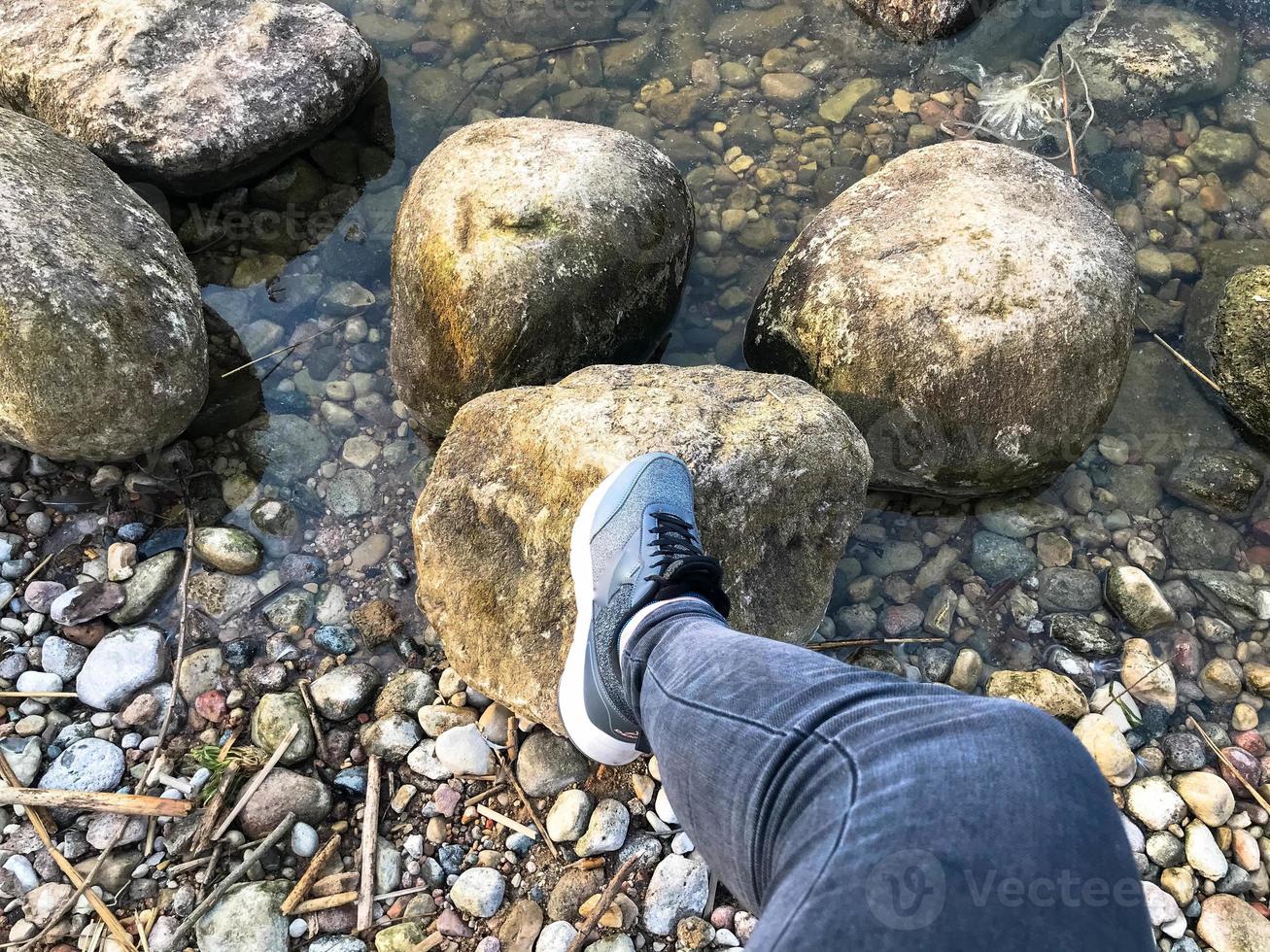 un pied dans une basket marche sur de grands pavés ronds de belles pierres naturelles dans l'eau, la mer, le lac, la rivière. concept tourisme, activités de plein air photo