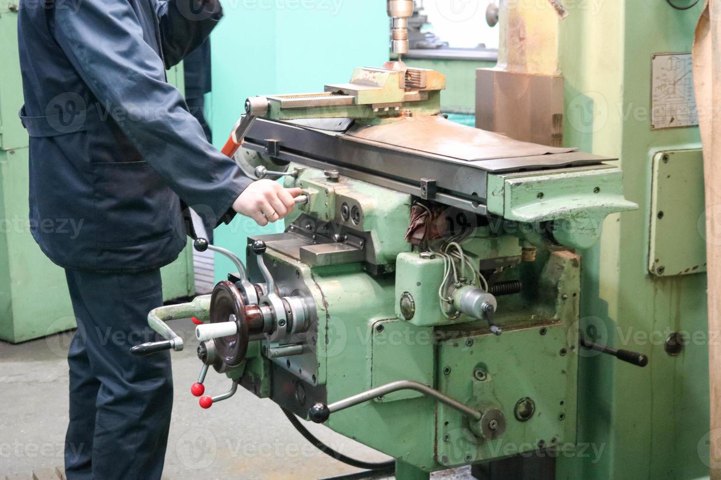 un travailleur masculin travaille sur un plus grand tour de serrurier en fer métallique, équipement de réparation, travail du métal dans un atelier d'une usine métallurgique dans une production de réparation photo