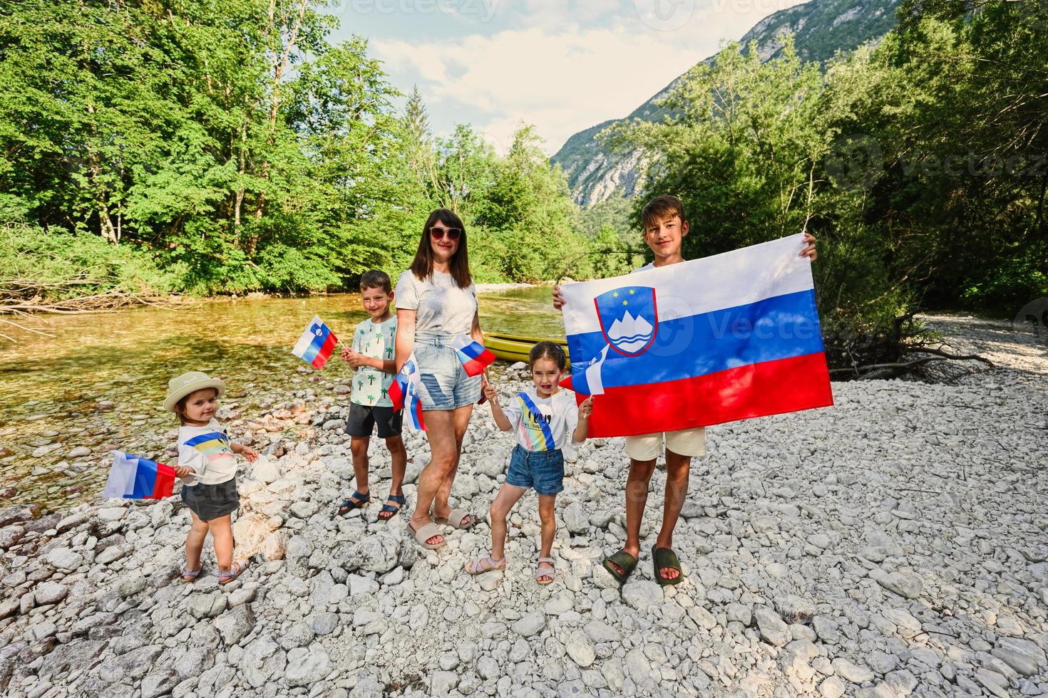 une mère avec des enfants tient des drapeaux slovènes sur la rive rocheuse d'une rivière calme dans le parc national du triglav, en slovénie. photo