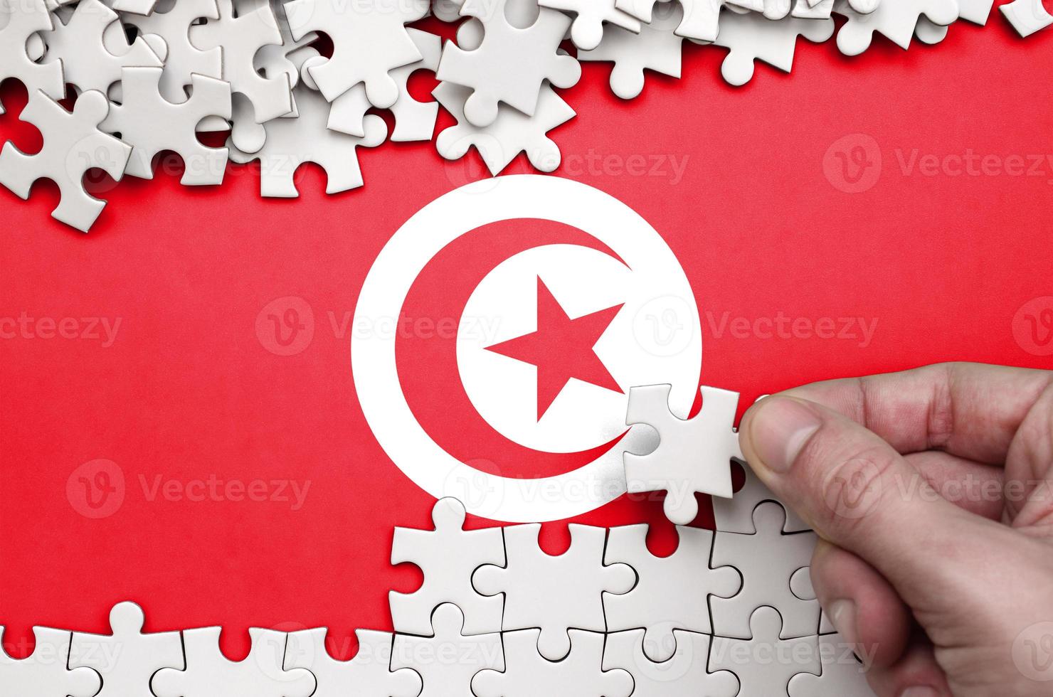 le drapeau tunisien est représenté sur une table sur laquelle la main humaine plie un puzzle de couleur blanche photo