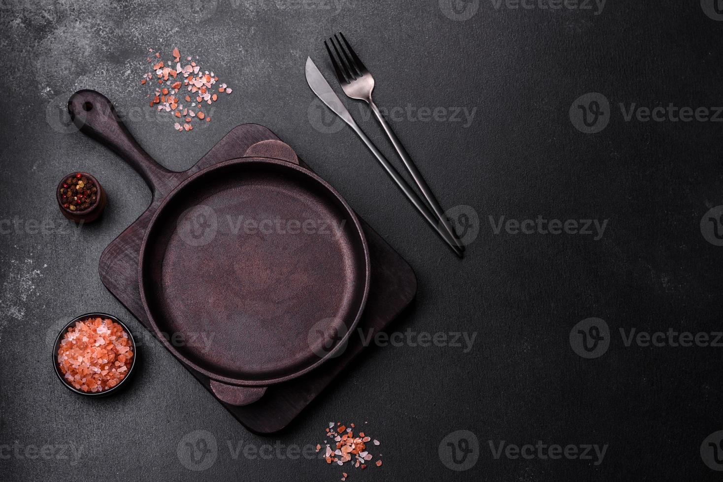 casserole vide en fer brun avec des ustensiles de cuisine sur un fond de béton foncé photo