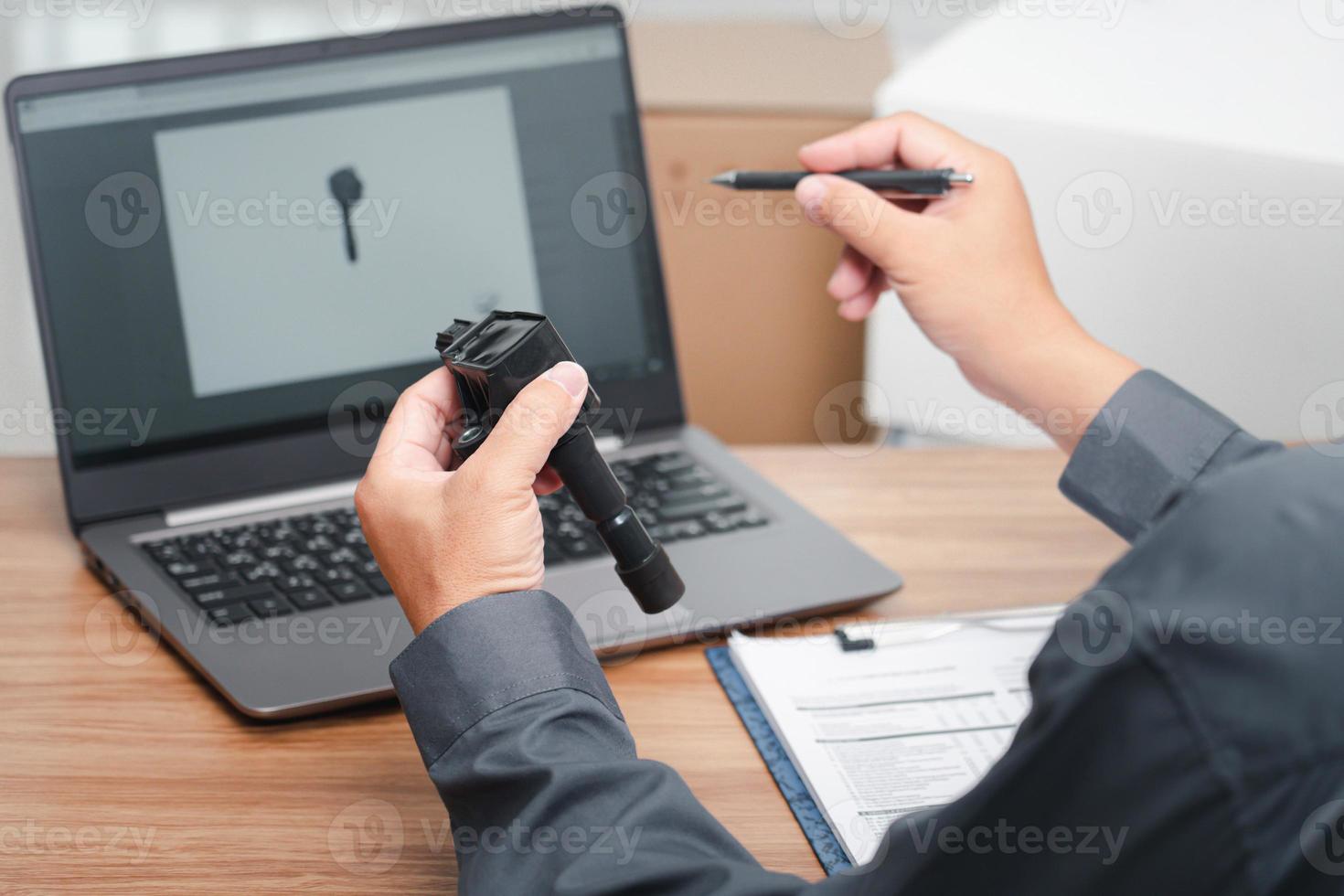 Main un homme tient l'ancien moteur à essence de bougie d'allumage de bobine et l'ordinateur portable vérifie l'exactitude des pièces de rechange avant de les retirer du concept de bureau de service de voiture de stock photo