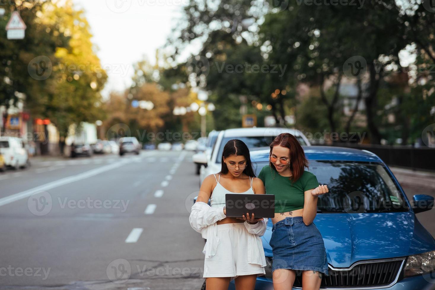 deux jeunes femmes avec un ordinateur portable près de la voiture photo