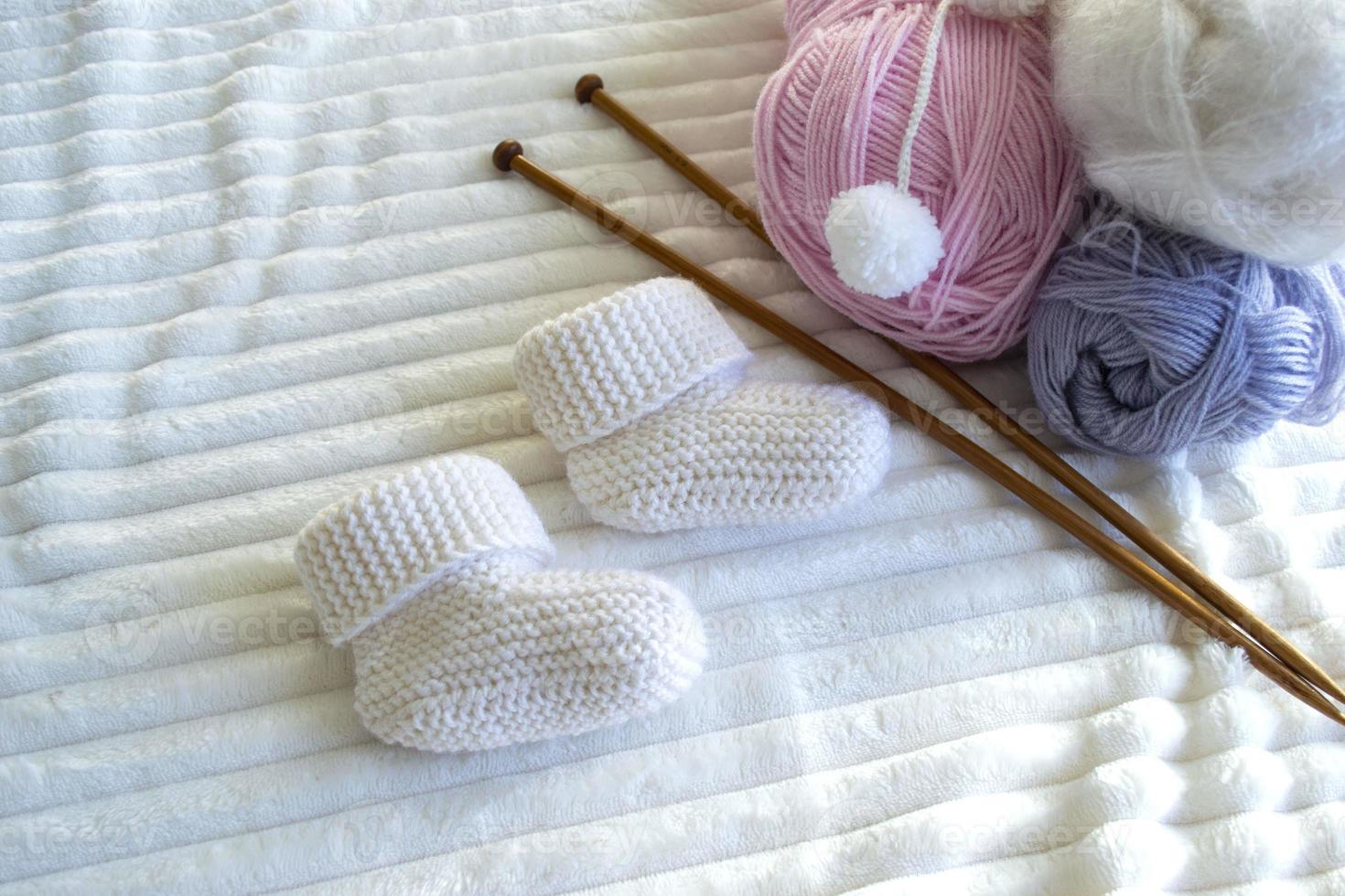 chaussons pour bébés blancs en laine tricotée et fil de laine mohair, aiguilles à tricoter. photo