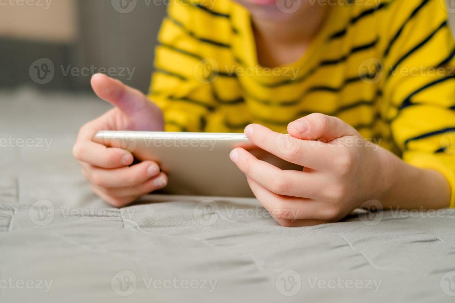 le garçon est allongé sur le canapé avec un téléphone dans les mains, gros plan. l'enfant joue à la maison au téléphone. loisirs avec le téléphone. photo