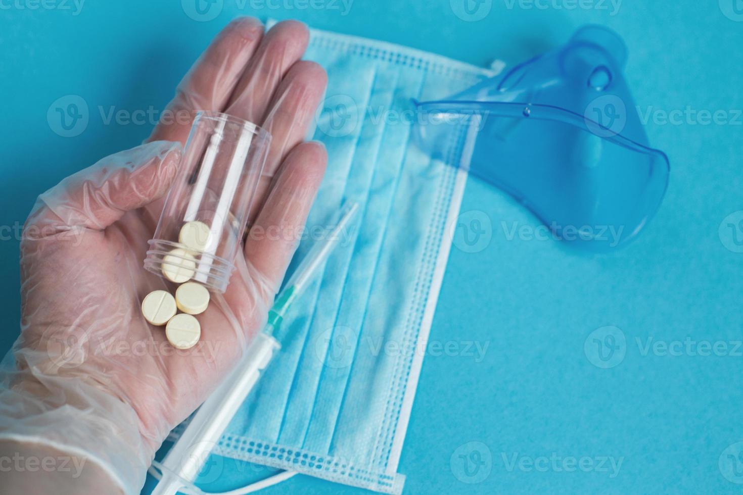 masque médical, seringue, masque pour inhalation et comprimés à proximité sur fond bleu. la main tient des pilules. coronavirus, grippe photo