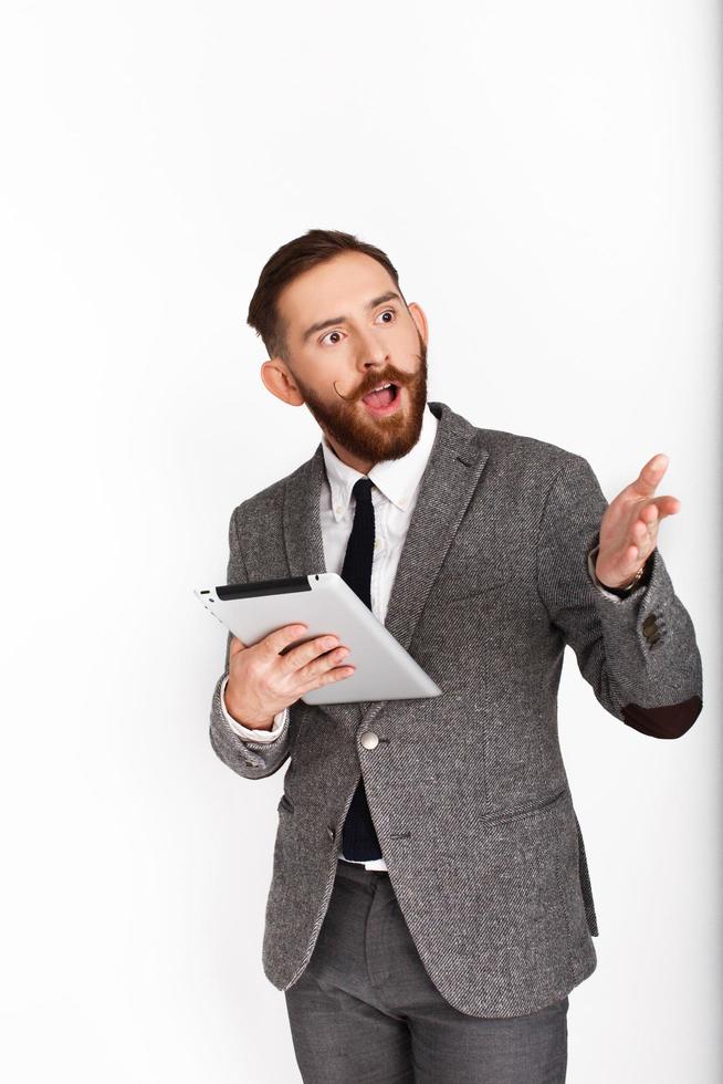 Homme barbu en costume gris parle tout en tenant une tablette sur fond blanc photo