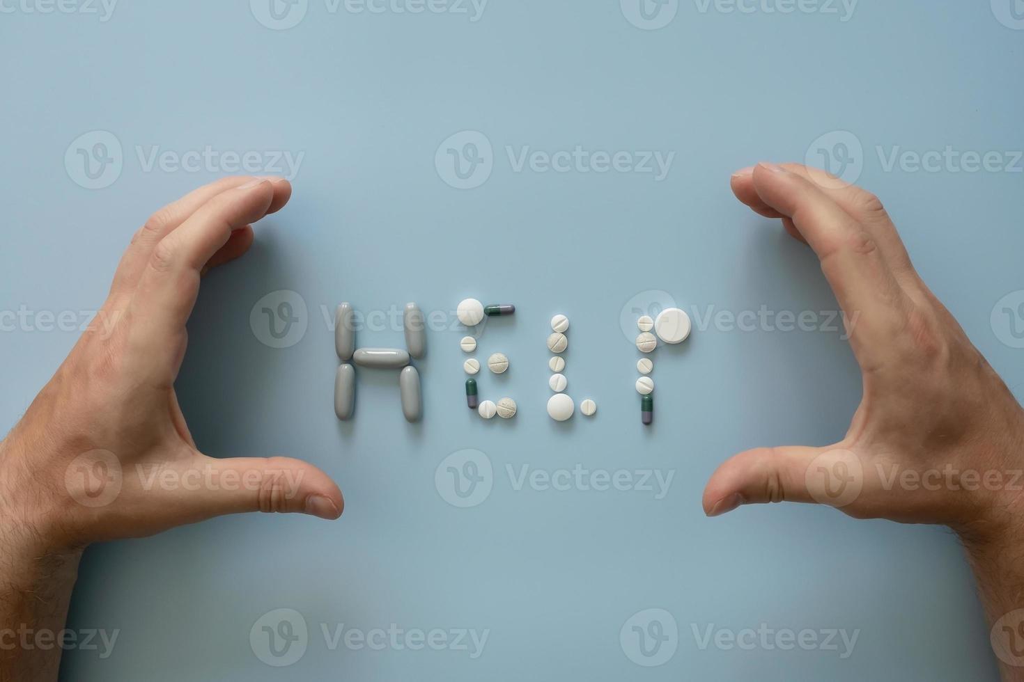 les mains ont disposé le mot aide de pilules assorties, sur fond bleu. concept médical ou tentation de drogues illégales. photo