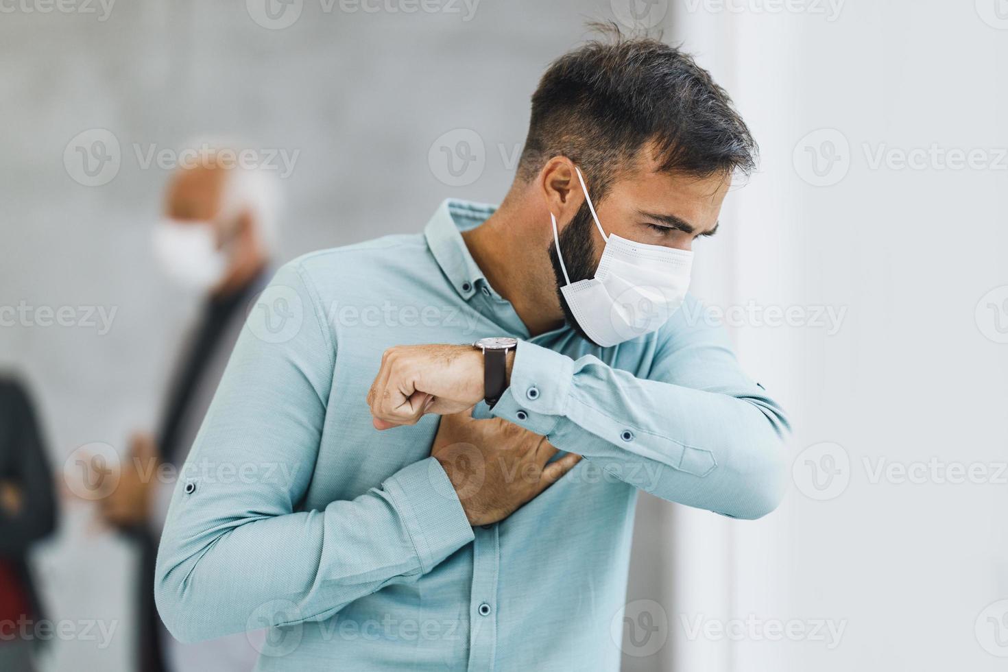 un homme d'affaires avec un masque de protection tousse au coude pendant la pandémie de coronavirus photo