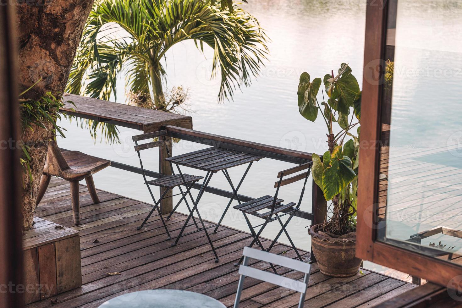 table et chaises en bois vides sur patio dans un jardin tropical au bord du lac photo