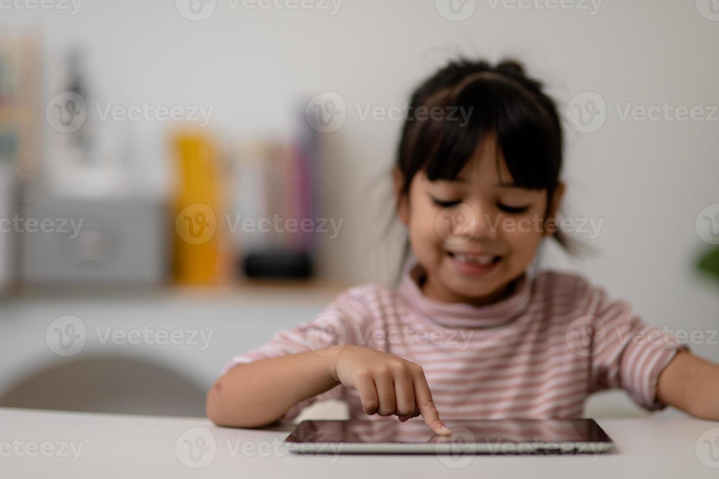 petite fille mignonne asiatique touchant l'écran de la tablette numérique sur la table photo