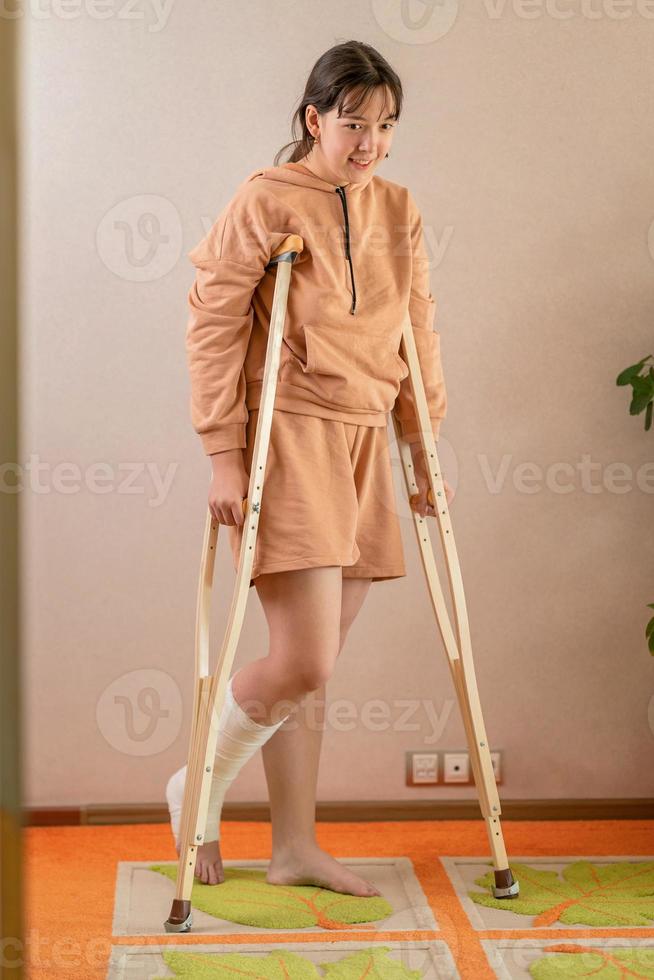 une fille avec une jambe cassée dans le plâtre se déplace dans l'appartement avec des béquilles photo