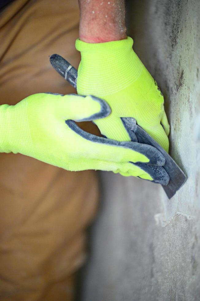 les champignons et les moisissures sont une manifestation d'un excès d'humidité dans la pièce, un homme avec une spatule enlève les champignons et les moisissures du mur. photo