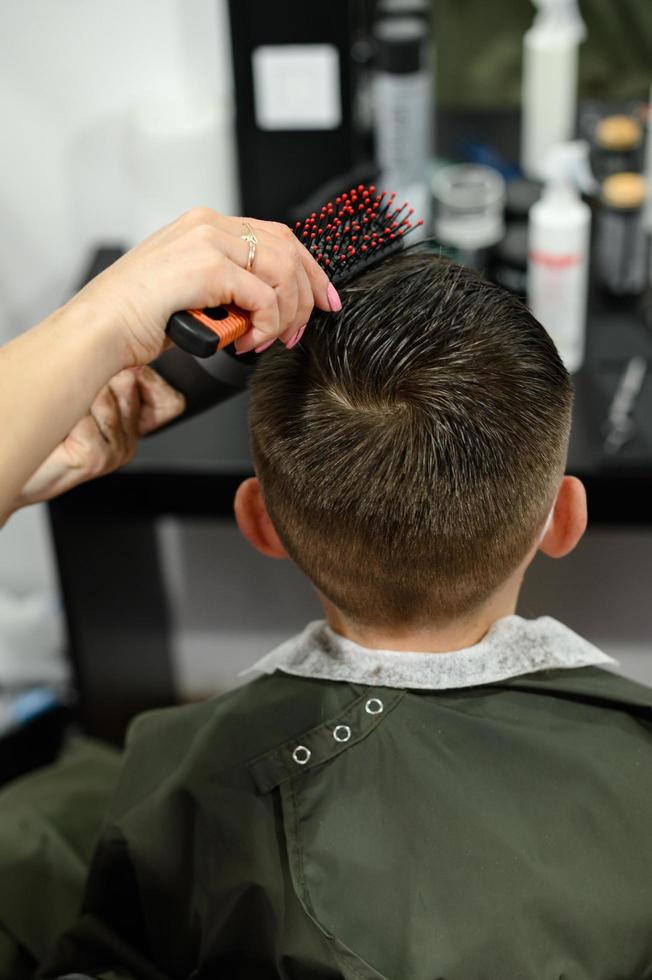 un adolescent se fait couper les cheveux pendant une pandémie au salon de coiffure, coupe de cheveux et sèche les cheveux après une coupe de cheveux. photo