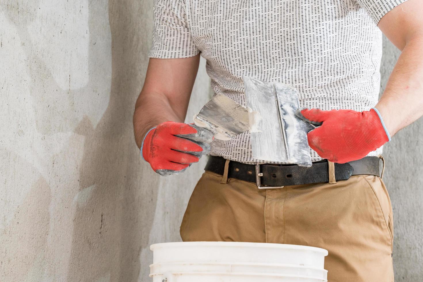 un homme avec une petite spatule applique de l'enduit à la chaux sur une grande spatule, de l'enduit à la chaux sur les murs et le plafond. photo