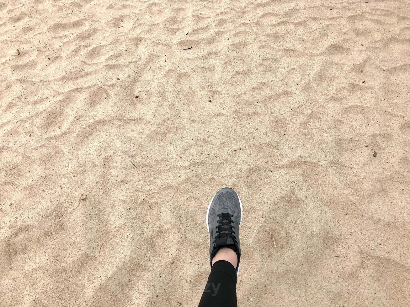 le pied dans la chaussure de botte grise fait un pas sur le fond d'un beau sable de plage chaud jaune doré naturel photo