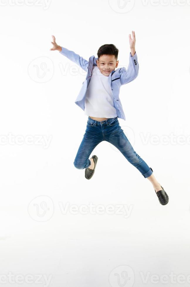 un garçon asiatique de 10 ans dans une veste décontractée saute intelligemment et joyeusement en regardant la caméra sur un fond blanc isolé. photo