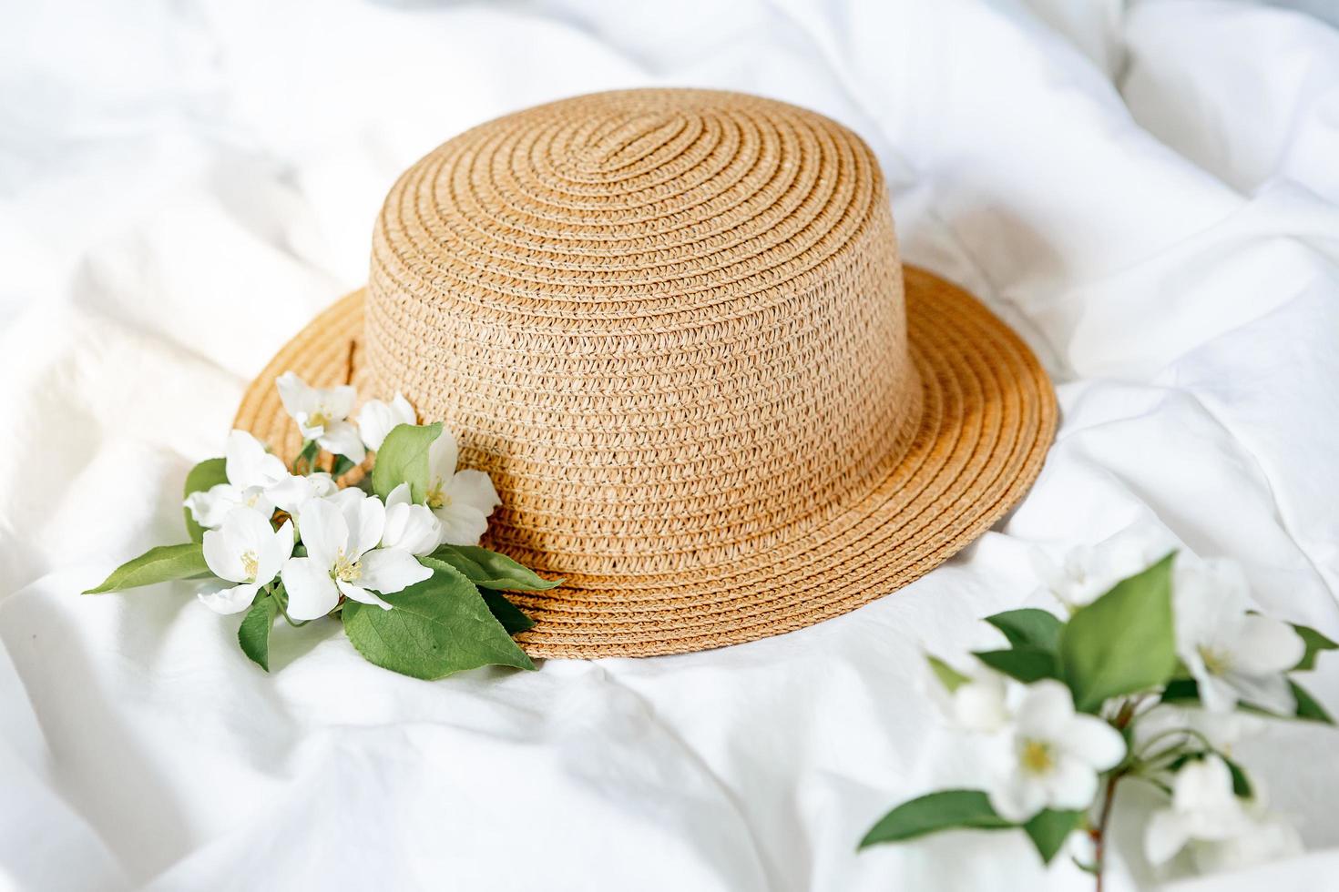 chapeau de paille sur le lit avec une branche de pommier en fleurs photo