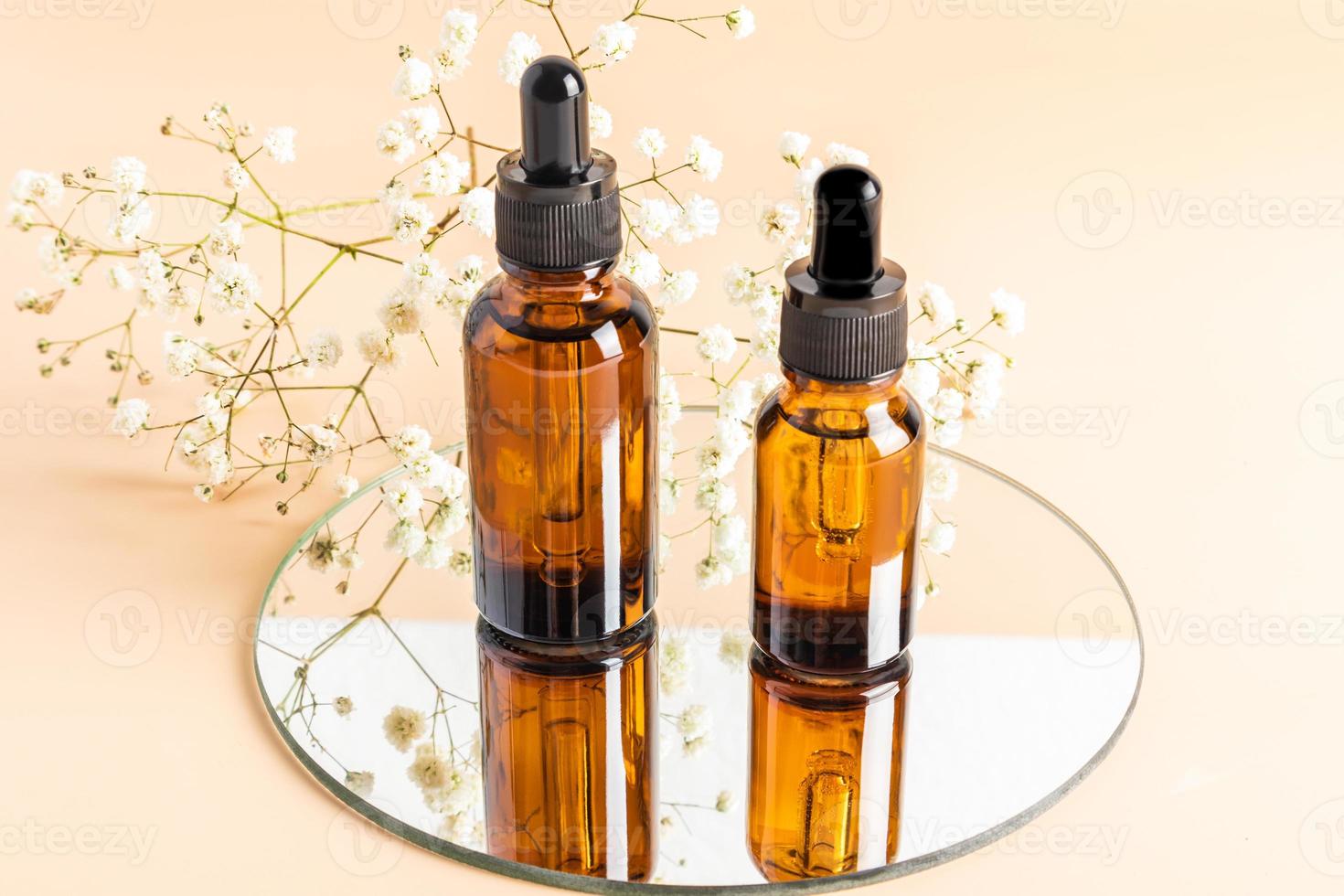 flacons cosmétiques en verre ambré avec un compte-gouttes sur un miroir rond avec une gypsophile blanche. vue de face. mise en page de la marque de cosmétiques. photo