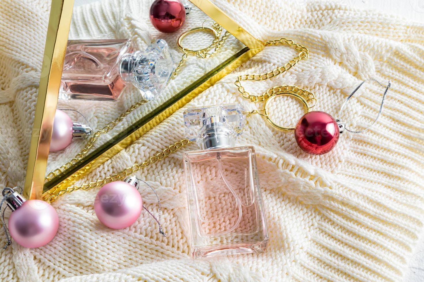 une bouteille de parfum féminin se reflète dans un miroir avec des boules de noël. fond beige tricoté. concept de cadeau, présentation de parfum. photo