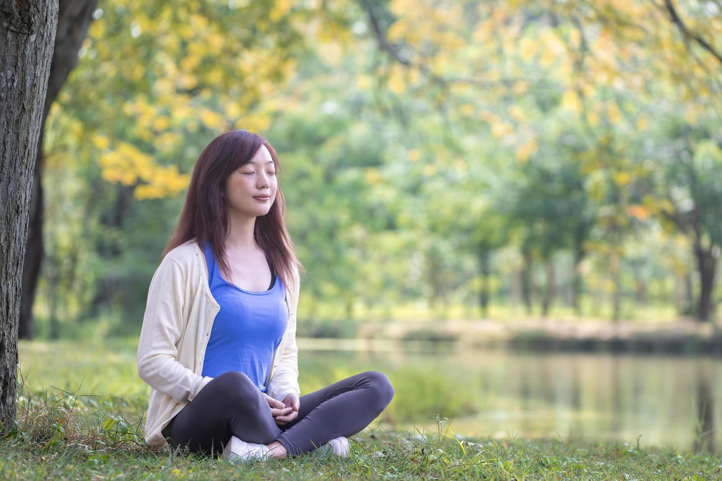 femme assise de manière relaxante et pratiquant la méditation dans le parc public pour atteindre le bonheur de la sagesse de la paix intérieure sous l'arbre en été photo