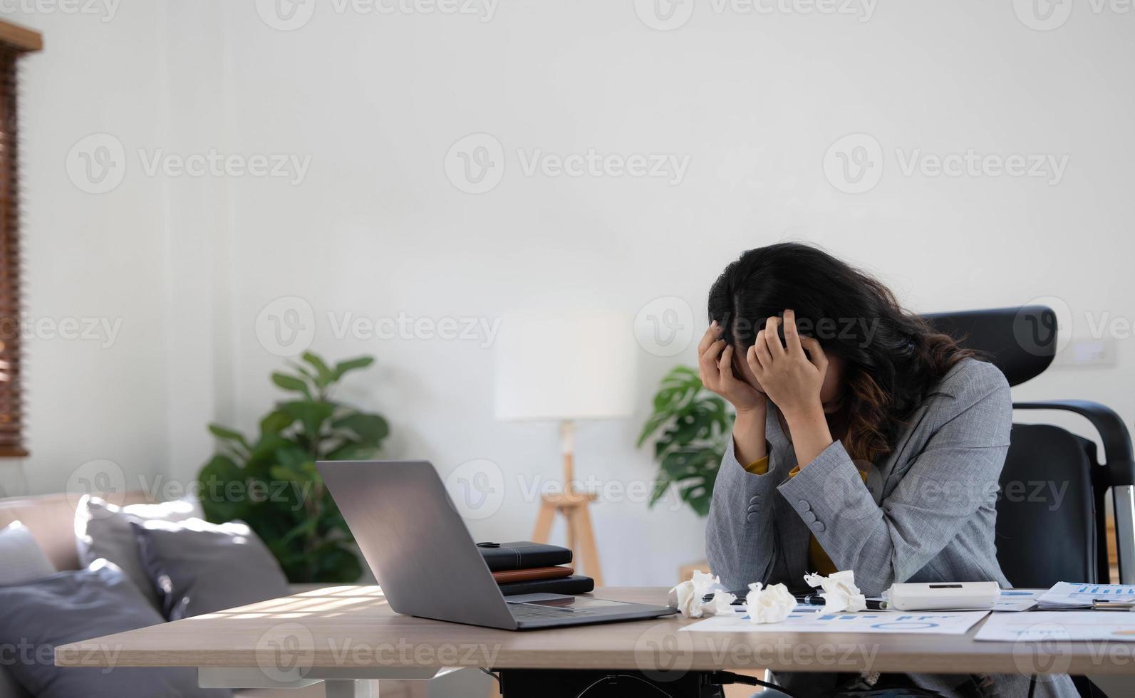 une femme d'affaires fatiguée et stressée travaille sur un ordinateur portable tout en étant assise à une table à la maison et tient sa main sur ses tempes, crise de migraine. freelance, travail à domicile. photo