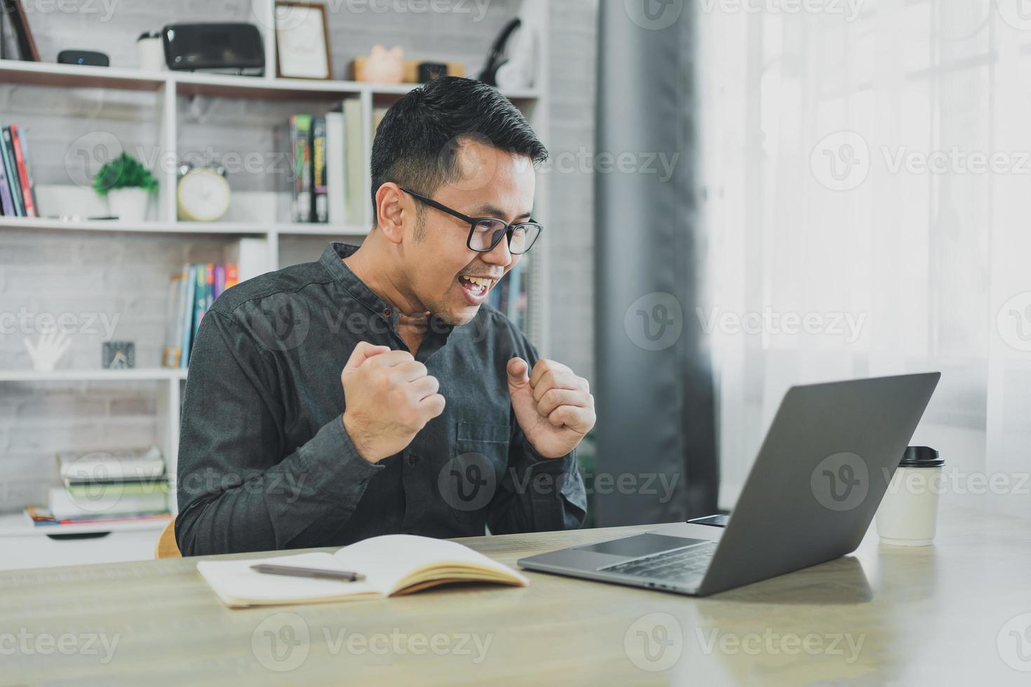 un homme asiatique indépendant d'affaires portant des lunettes sourit et est heureux du succès tout en travaillant en ligne sur un ordinateur portable et en célébrant à la maison ou n'importe où. succès de travail joyeux et bonheur, concept d'entreprise. photo