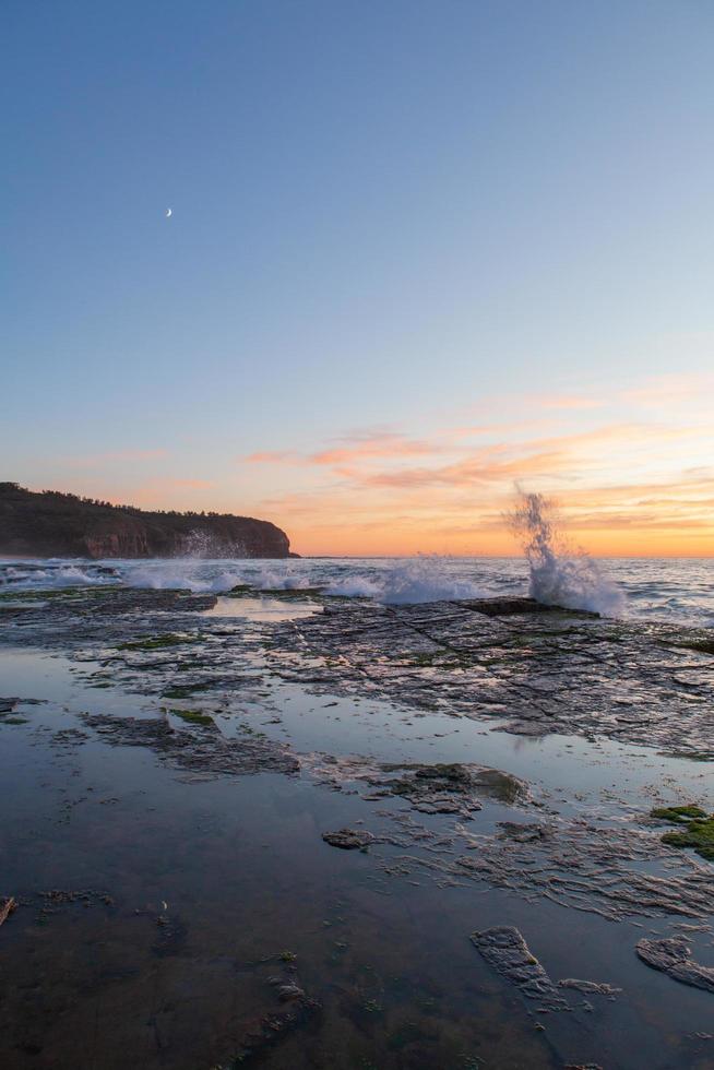 vagues éclaboussant sur le rivage au coucher du soleil photo