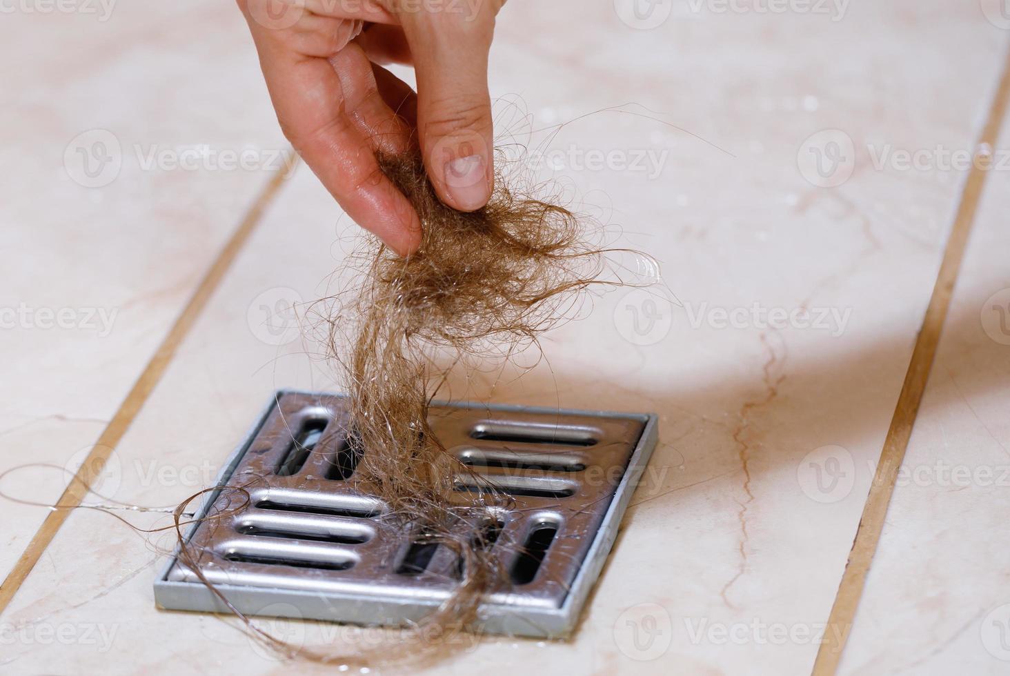 femme enlevant la touffe de cheveux du drain de douche photo