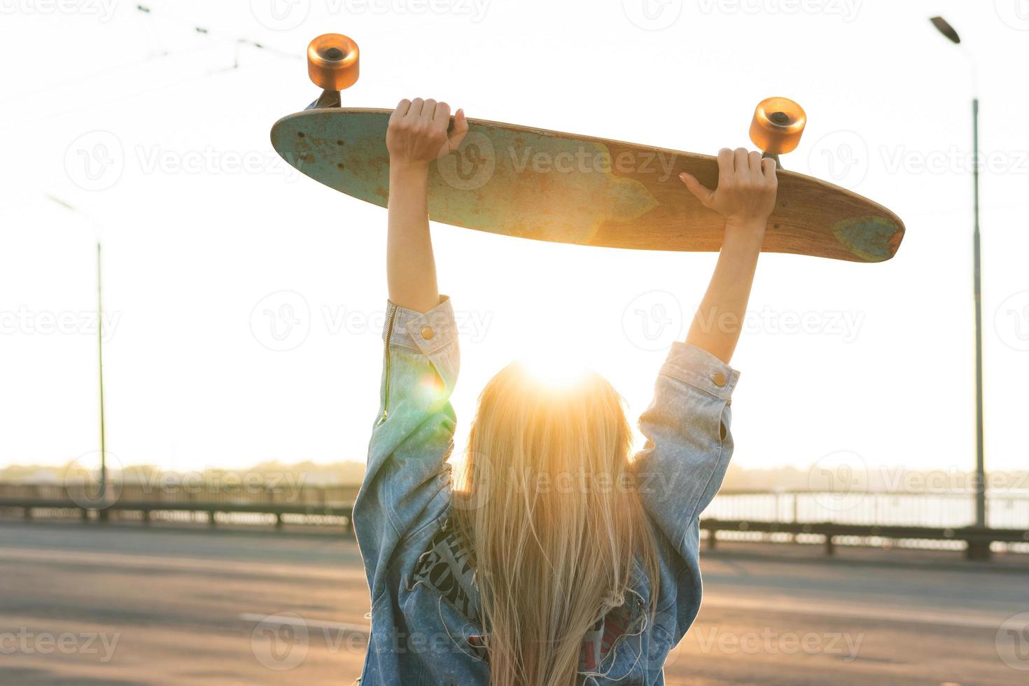 femme insouciante avec un longboard sur un pont au coucher du soleil photo