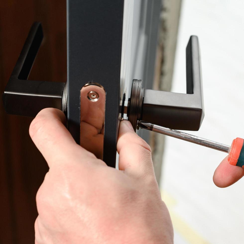 un homme installe une poignée de porte dans une porte, menuiserie à la maison. photo