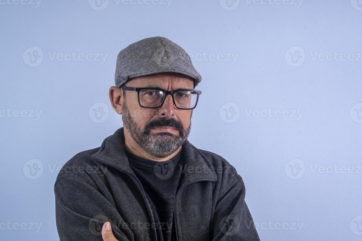 portrait d'homme barbu de 60 ans sur fond bleu avec chapeau et lunettes photo