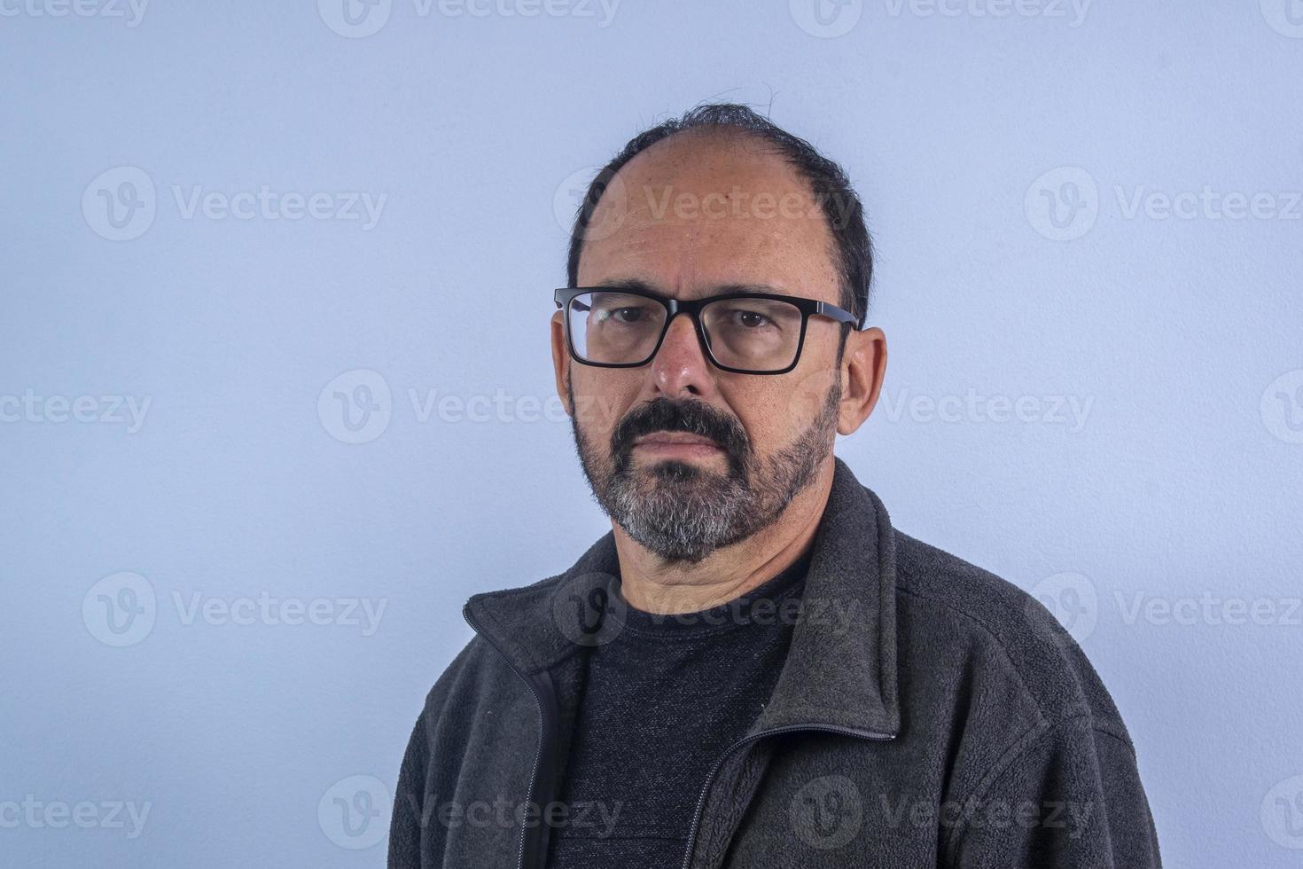 portrait d'homme barbu de 60 ans sur fond bleu avec chapeau et lunettes photo