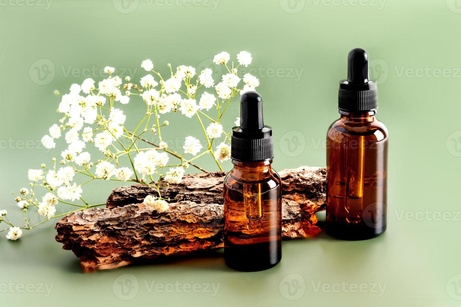 deux flacons avec un compte-gouttes avec un sérum pour le soin de la peau du visage sur fond d'écorce d'arbre et de fleurs. photo