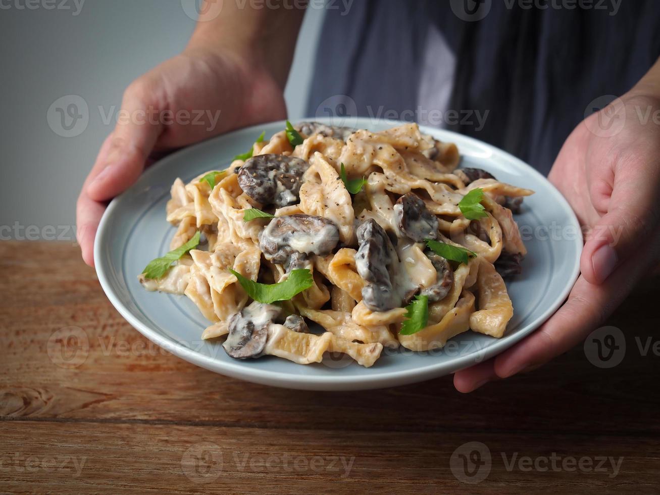 main de femme tenir un plat de pâtes faites maison avec champignons champignons et sauce carbonara. photo