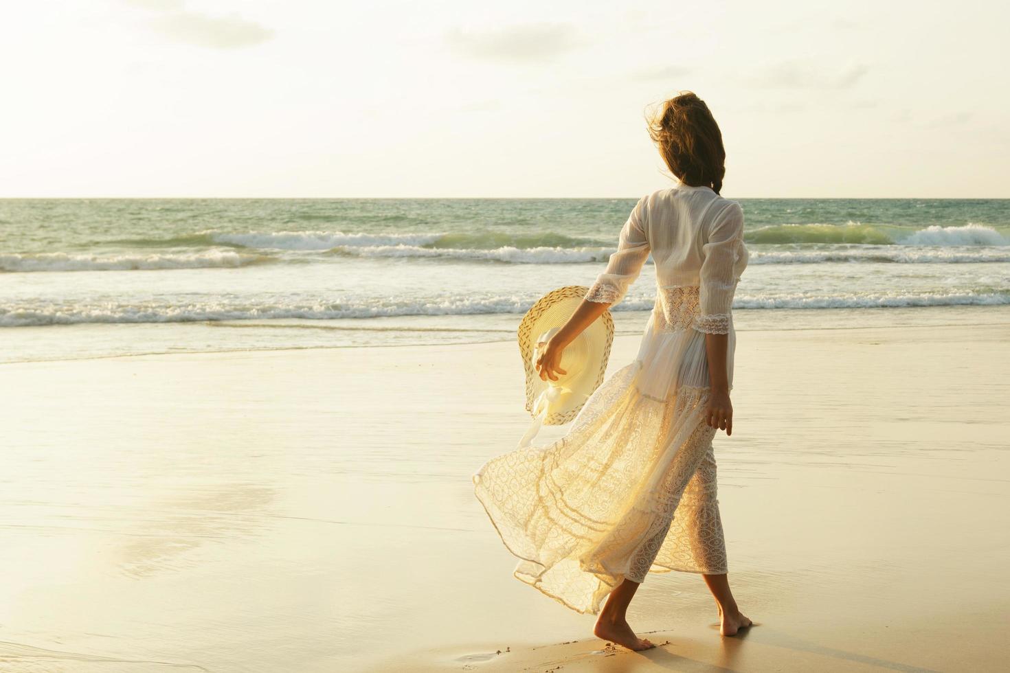 femme vêtue d'une belle robe blanche marche sur la plage au coucher du soleil photo