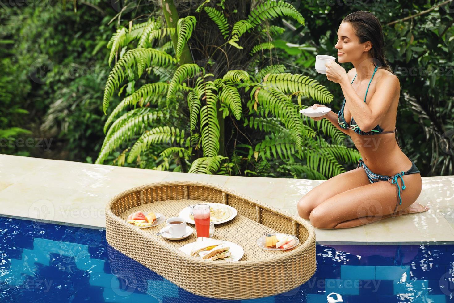 jeune femme heureuse avec un petit déjeuner flottant dans la piscine photo