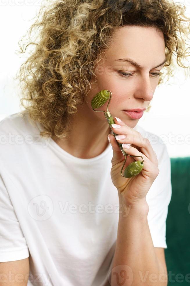 belle femme faisant un massage du visage avec un dermaroller de jade à la maison photo