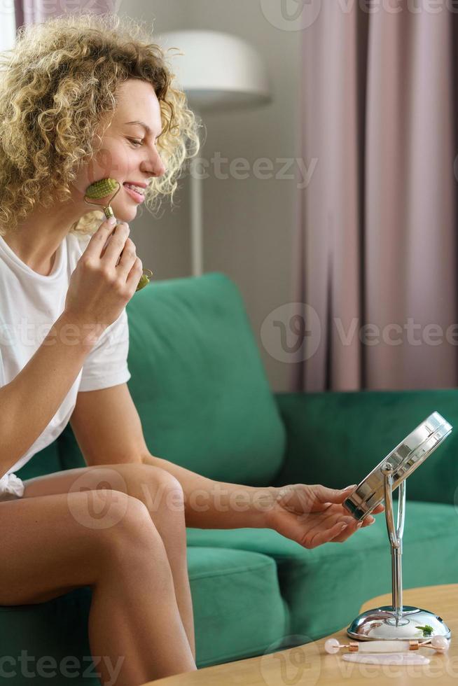 belle femme faisant un massage du visage avec un dermaroller de jade à la maison photo