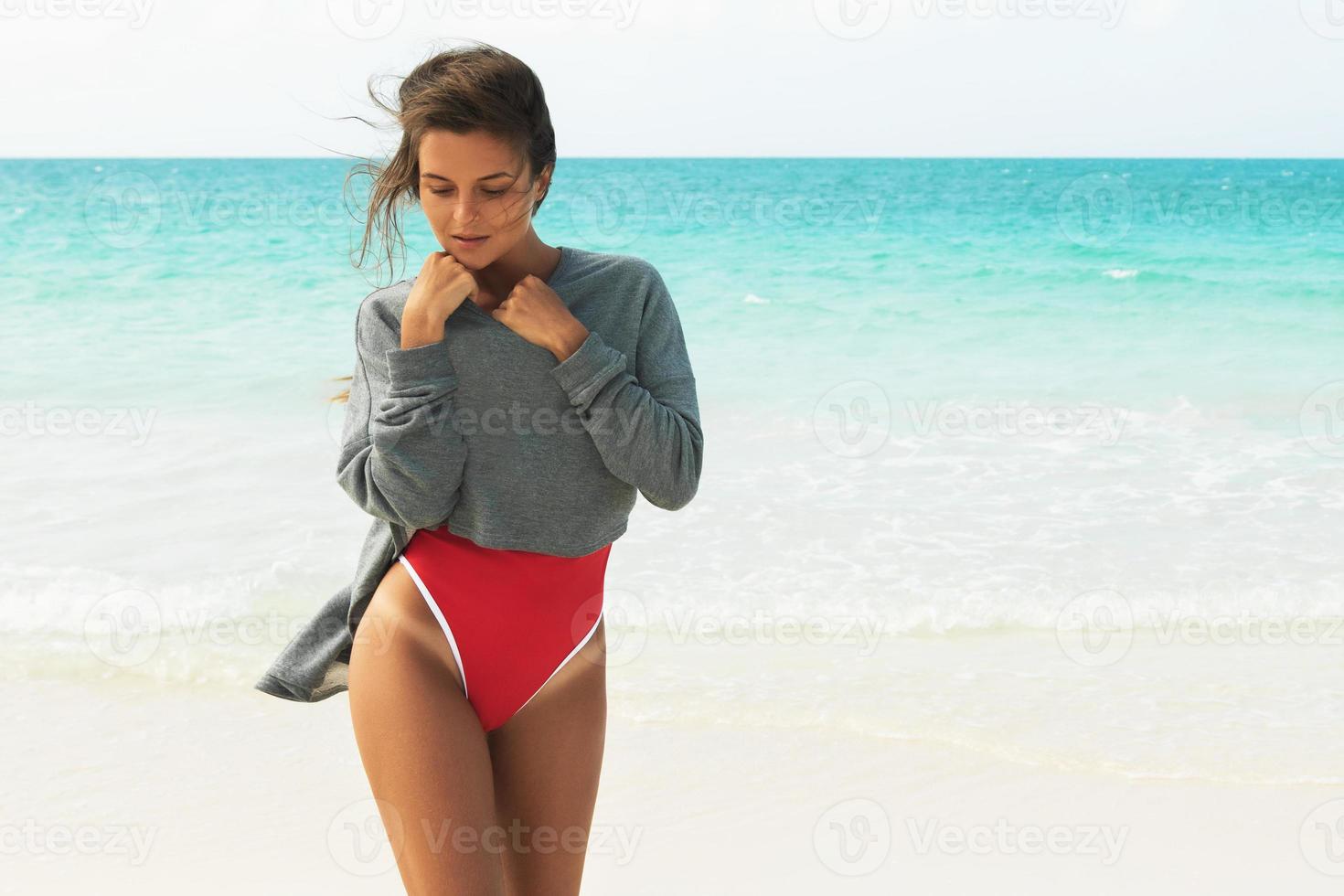 belle femme portant un maillot de bain rouge et un sweat-shirt marchant sur une plage photo