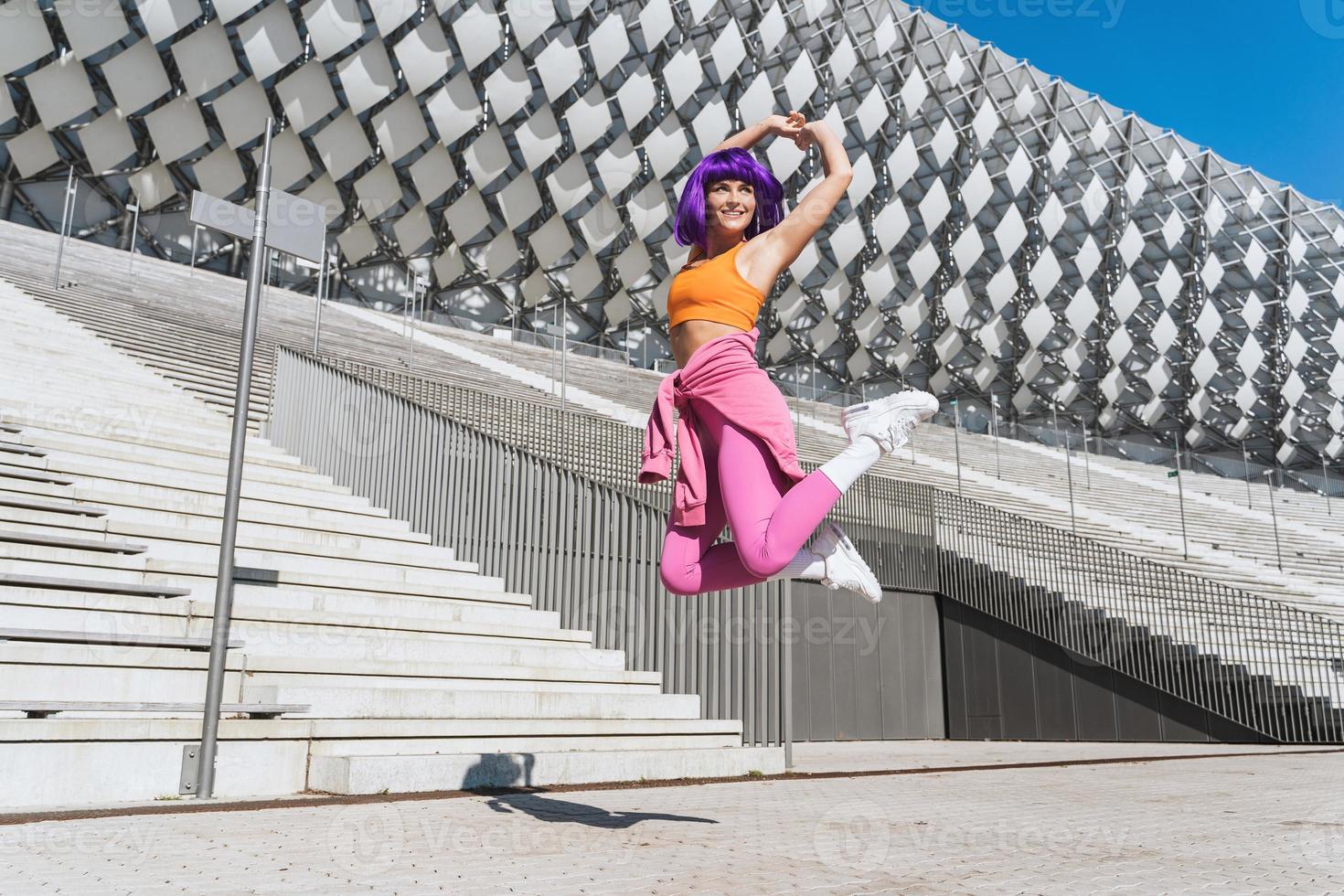 femme insouciante portant des vêtements de sport colorés sautant dans la rue pendant la journée d'été photo