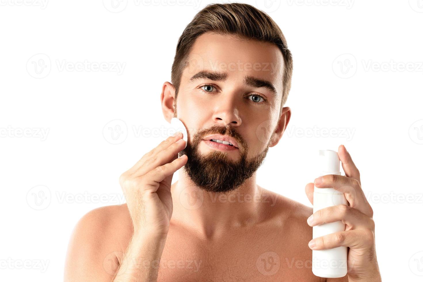 jeune bel homme nettoie son visage avec un coton photo