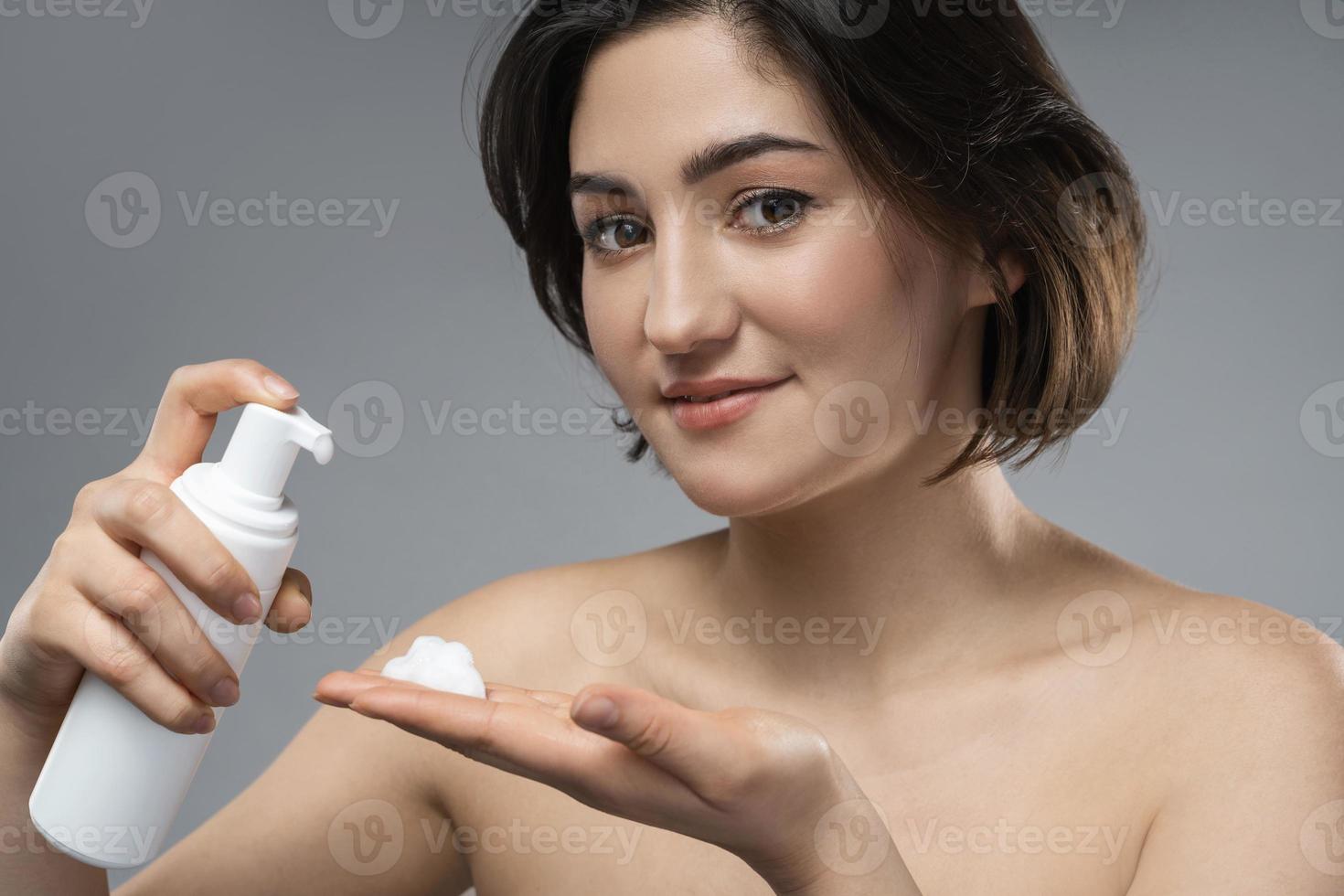 belle femme brune à la peau lisse avec une bouteille de mousse nettoyante photo