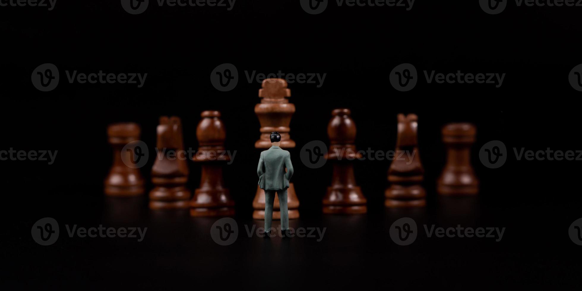 chiffres homme d'affaires debout devant des échecs en bois sur fond noir isolé. concept d'analyse et de stratégie d'entreprise. entrer dans la startup, nouvel acteur du business photo