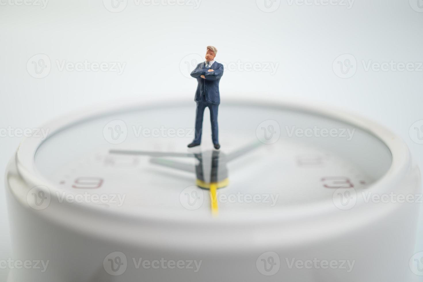 les hommes d'affaires de la figure pensent et se tiennent sur le cadran blanc de la montre près du cadran de la montre indiquant l'heure. notion de gestion du temps. photo