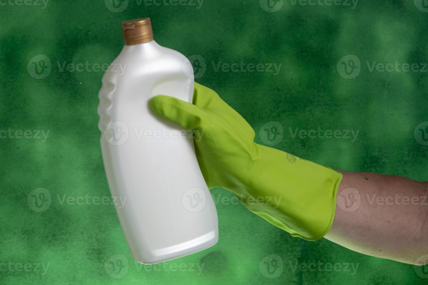 main avec gant de protection tenant l'emballage des produits de nettoyage utilisés pour l'hygiène domestique photo