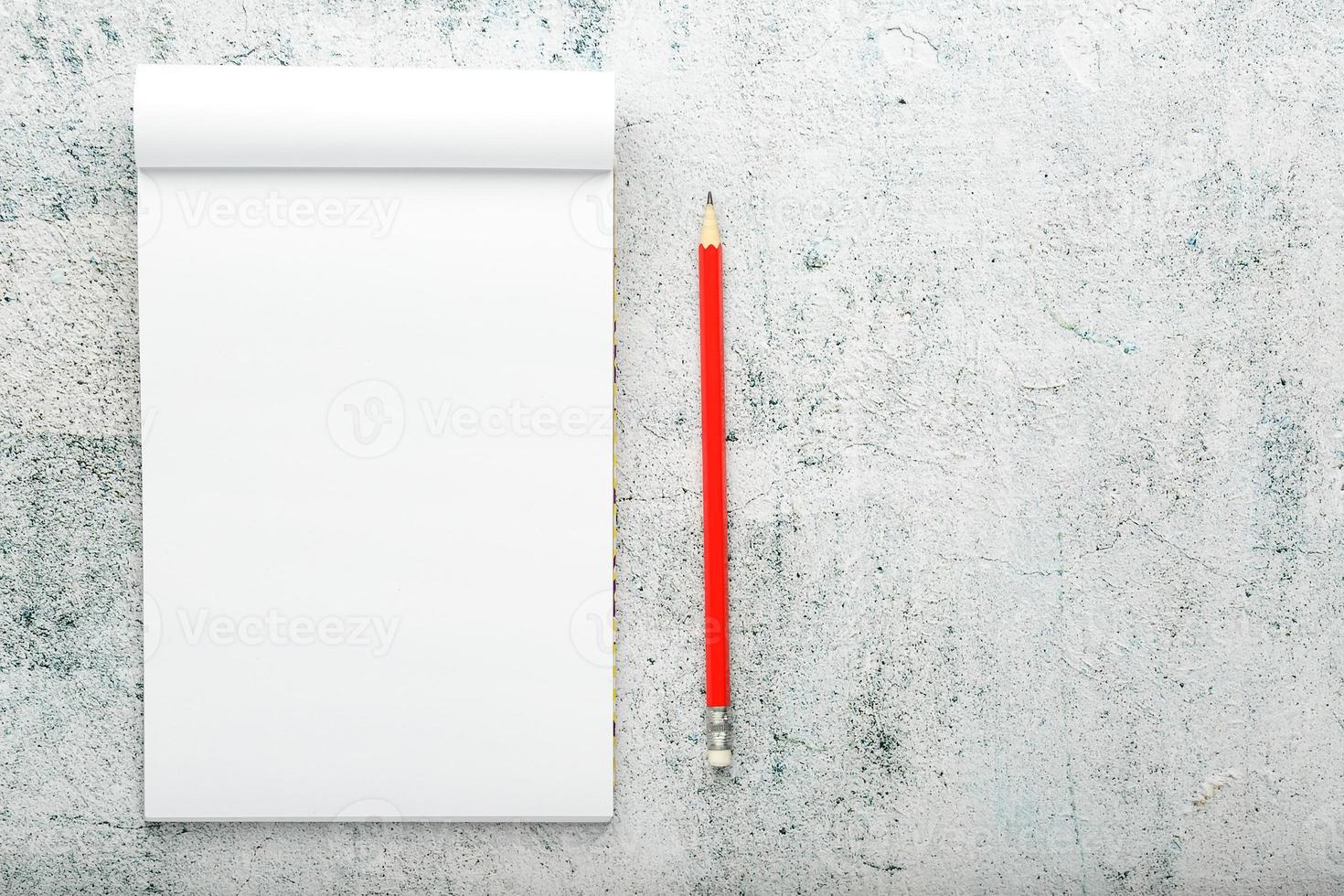 bloc-notes avec un crayon rouge sur fond de mur en plâtre blanc, pour l'éducation, écrire des objectifs et des actes photo